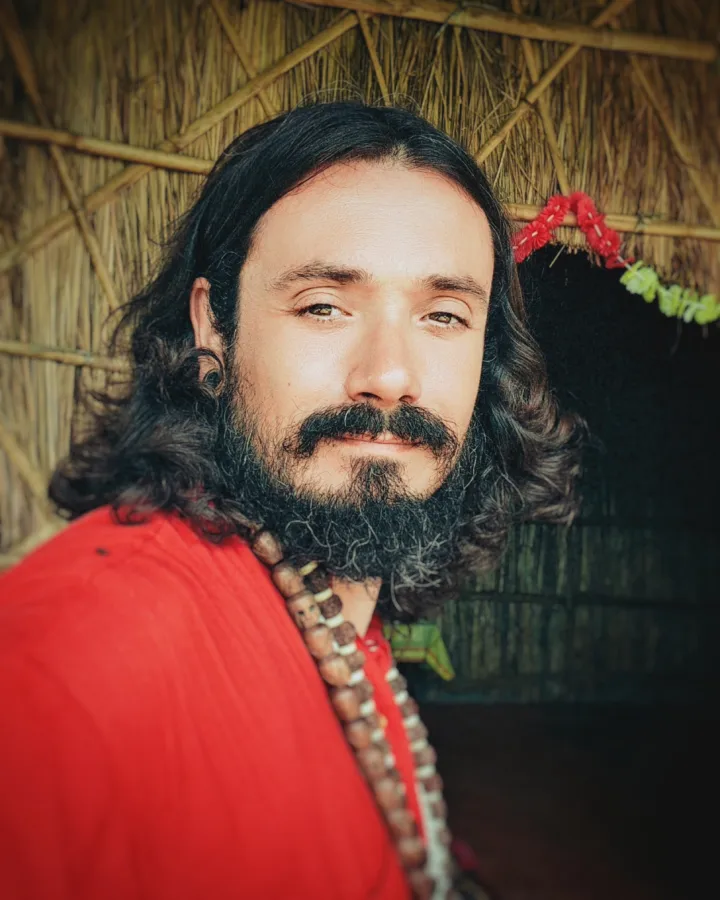 Sri Satpremananda Maharaj en robe rouge, dans une hutte de chaume